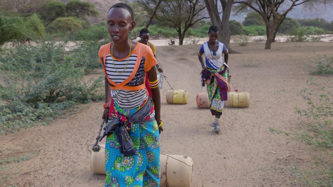 气候change.drought.water危机。特写镜头前视图。一名非洲妇女走着用塑料容器打水回家，这些塑料容器是从由于持续干旱而从深井中收集的。肯尼亚视频素材