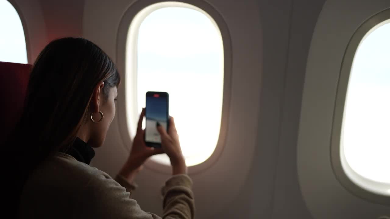 年轻女子乘飞机旅行，透过窗户拍照视频素材