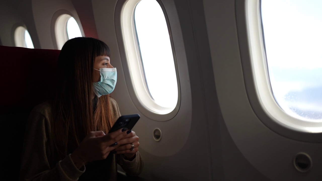 年轻女子戴着口罩坐飞机，看窗户，还在用手机视频素材