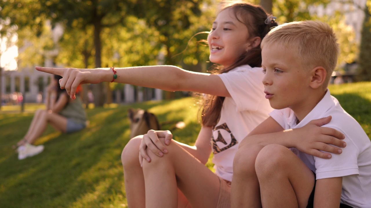 一个小男孩和一个小女孩在公园里坐在绿草地上聊天。视频素材
