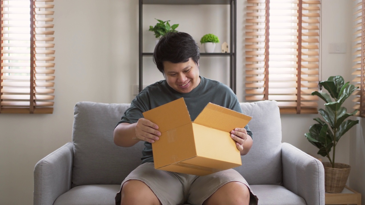 快乐的男人坐在沙发上打开收到的盒子，微笑着看里面视频素材