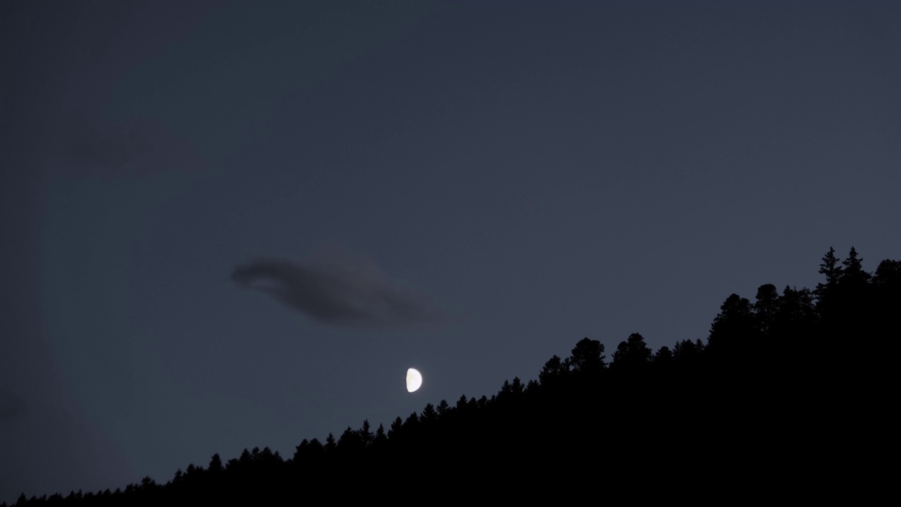 半个月亮的时间推移隐藏在山与树木和少数云彩4K视频素材