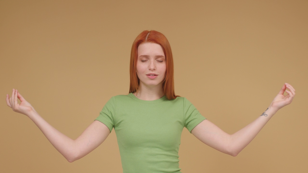 穿着t恤的姜黄色女人正在冥想，张开双臂让自己平静下来视频下载