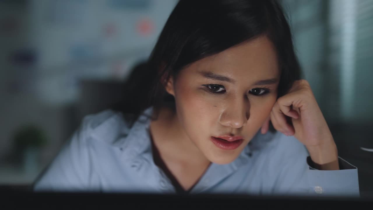 年轻的亚洲女企业家沮丧地看着电脑屏幕，深夜在家庭办公室用笔记本电脑工作。视频素材