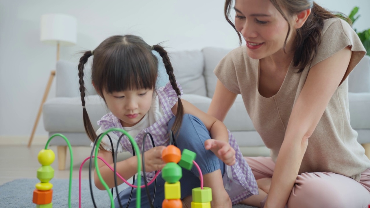亚洲美丽慈爱的妈妈在家里和女儿玩教育游戏。漂亮的女人父母花空闲时间与年轻的小女孩孩子花时间学习和发展技能与儿童的玩具。视频素材