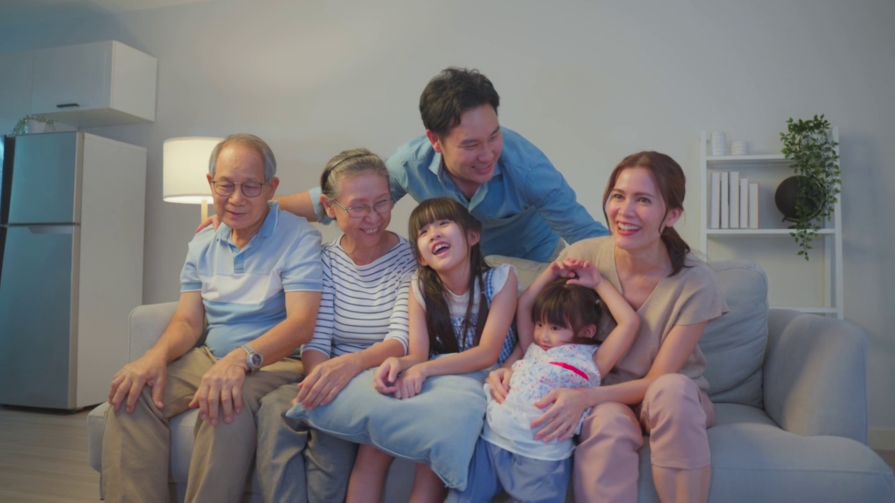 亚洲爱的家庭在家里的客厅一起看足球比赛。年迈的祖父母和年轻的夫妇带着小女儿坐在沙发上看着电视上的体育比赛，感到很兴奋。视频下载