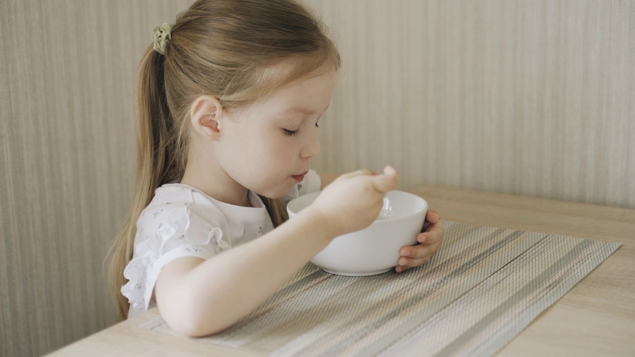 女孩坐在桌旁吃牛奶粥。视频素材