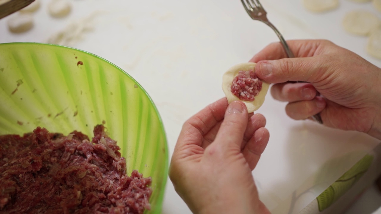 女性手用叉子从大碗里挑肉末，然后把饺子馅放进面团里。视频下载