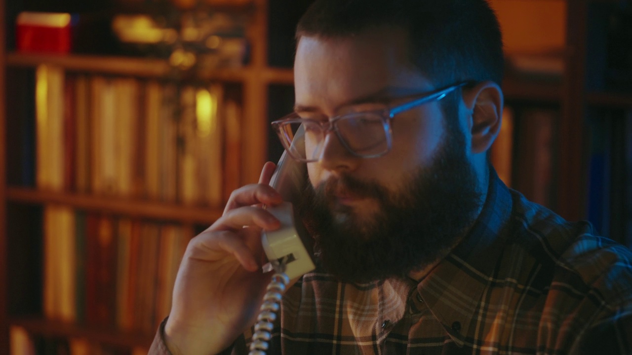 尴尬的书呆子年轻人戴着眼镜打电话，用老式的有线电话聊天视频下载