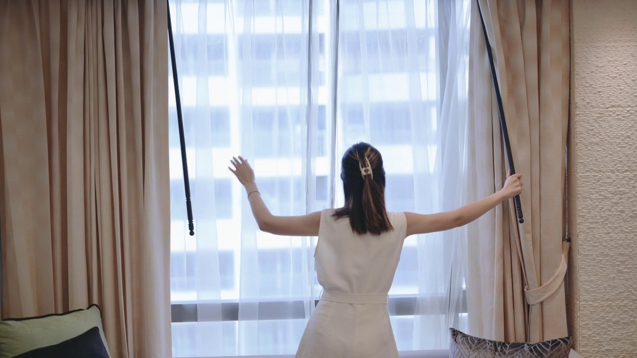 亚洲女性的后视图打开窗帘和看窗外的公寓视频素材