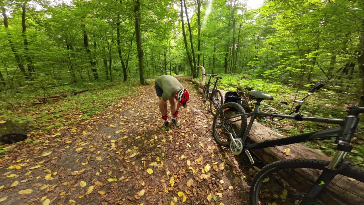 一名戴着防护头盔的男子在森林里骑自行车前整理袜子。视频素材