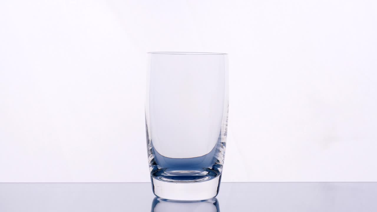 浇注的饮用水。近距离将纯化的新鲜洁净饮用水倒入玻璃杯中，白色背景下的水在玻璃杯中飞溅，柔焦4K。饮酒、健康、自然的概念视频素材