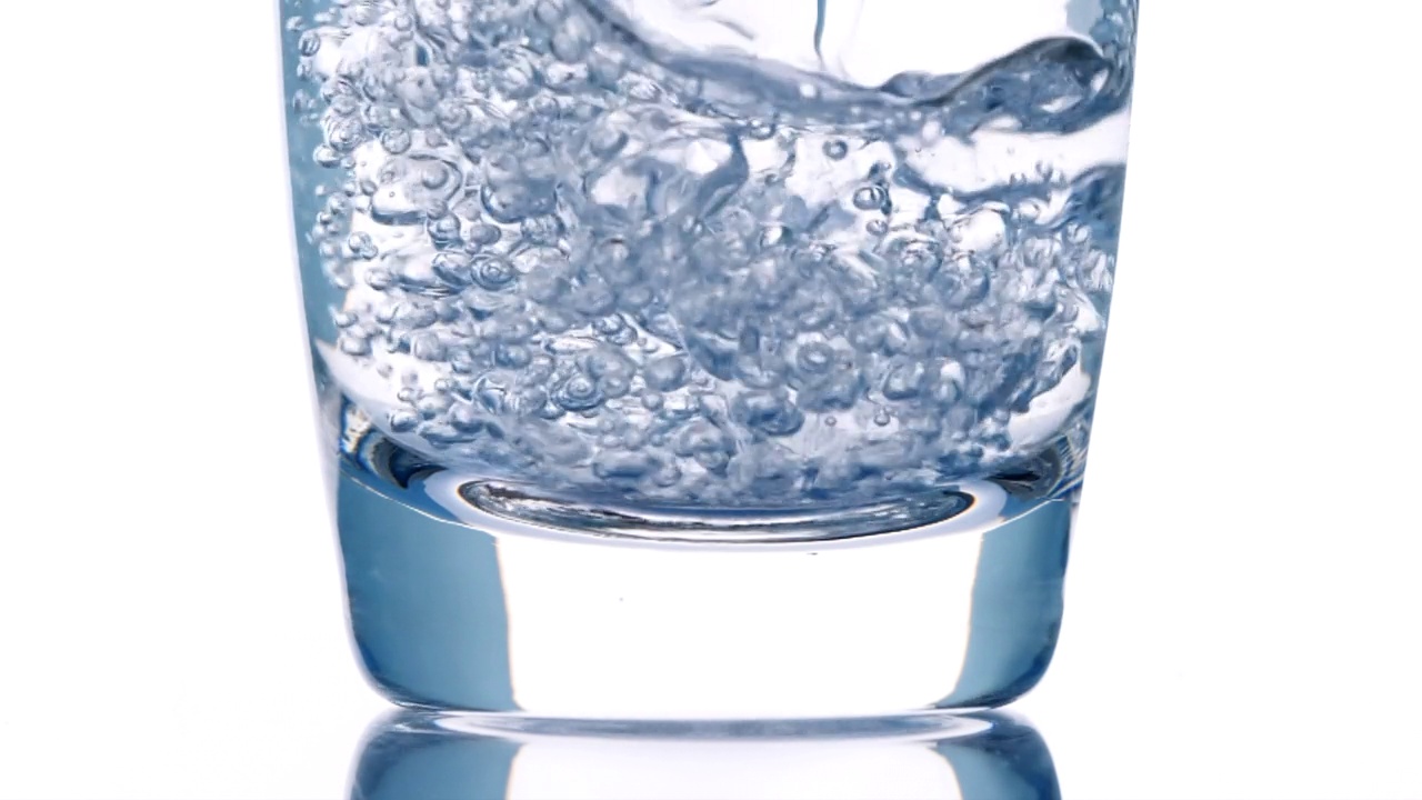 浇注的饮用水。特写将纯化的新鲜干净的饮用水倒入玻璃杯中，水在白色背景上溅起，用慢动作柔和聚焦。饮酒、健康、自然的概念视频素材