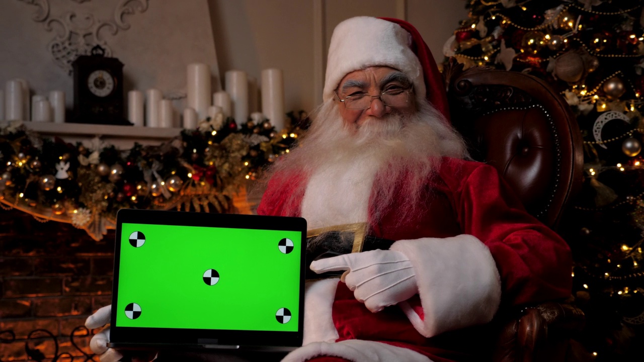 笑眯眯的圣诞老人指着笔记本电脑的绿色屏幕，圣诞购物视频下载