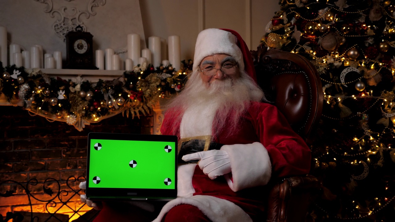圣诞老人微笑着用手指着笔记本电脑的绿色屏幕，圣诞购物视频下载