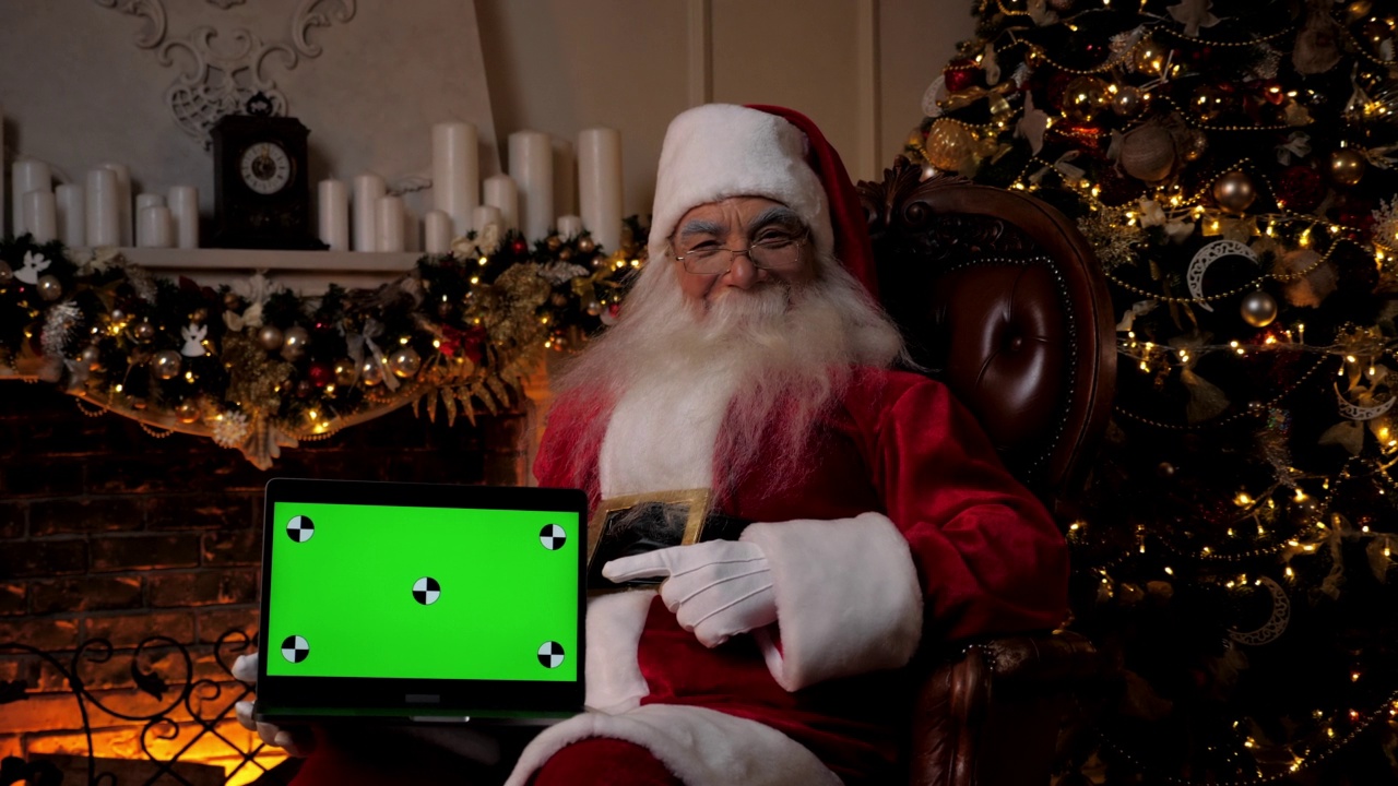 笑眯眯的圣诞老人指着笔记本电脑的绿色屏幕，圣诞购物视频下载