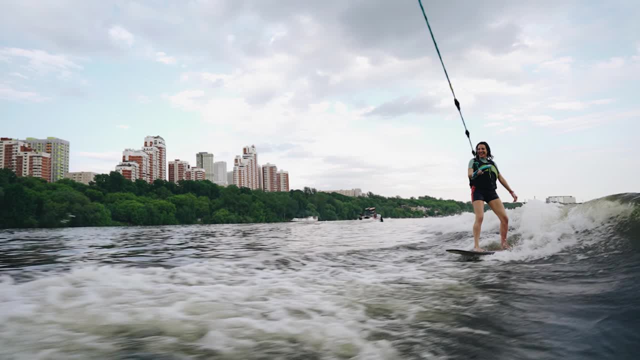 一个欢快的女孩抓着绳子在船后移动。海浪追逐着她。视频素材