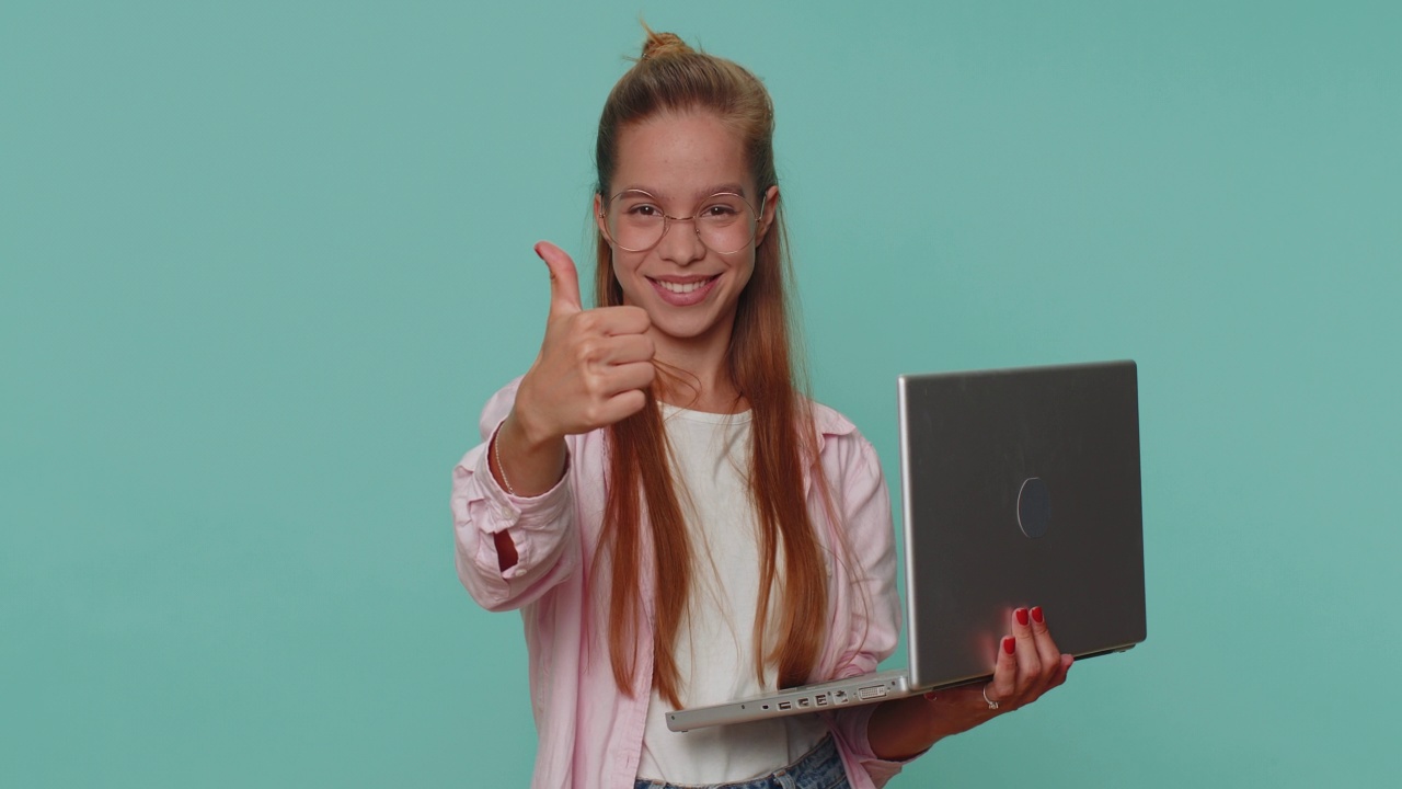 一个女孩在笔记本电脑上上网，对着镜头竖起大拇指，给出积极的反馈，像是中了彩票视频素材