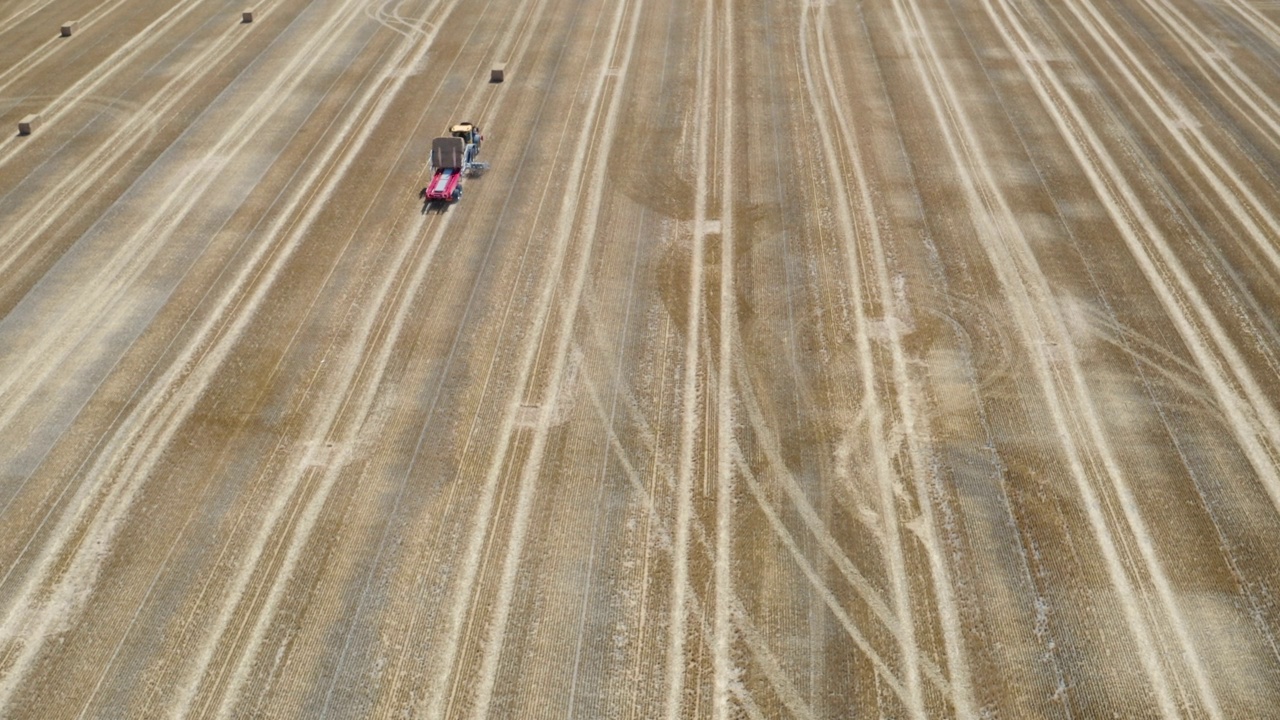 无人机拍摄的拖拉机在最近收获的农田里捡起捆视频素材