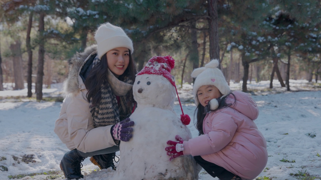 一个年轻的母亲和女儿在雪地里堆雪人视频素材