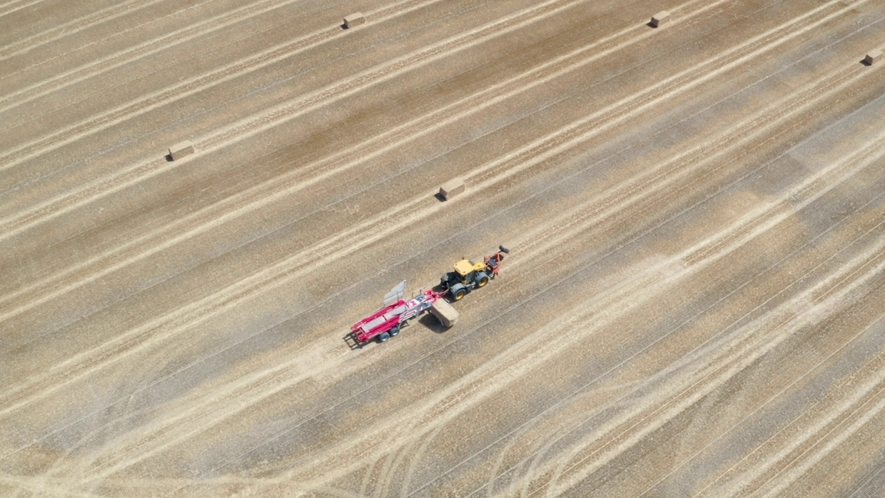 无人机拍摄的拖拉机在最近收获的农田里捡起捆视频素材