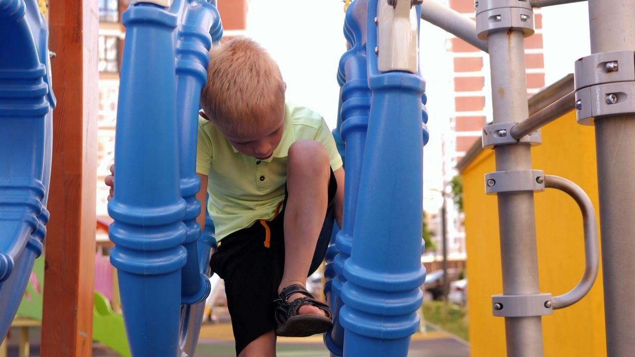 一个小男孩在操场上玩，他爬过大的塑料圈。视频下载