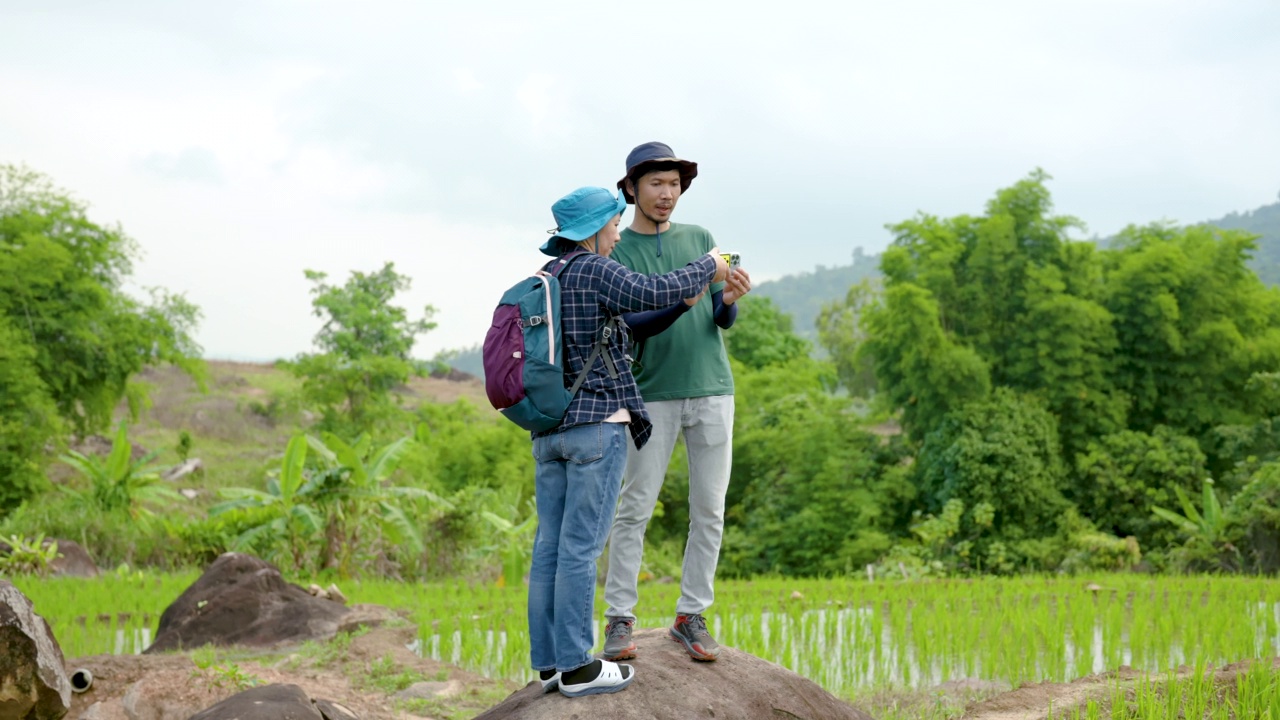 4K，年轻的亚洲人，走着走着，发现一片刚刚种下的软软的田地，他们两个激动地看到了美丽的绿色稻田，准备拿起手机拍照。视频下载