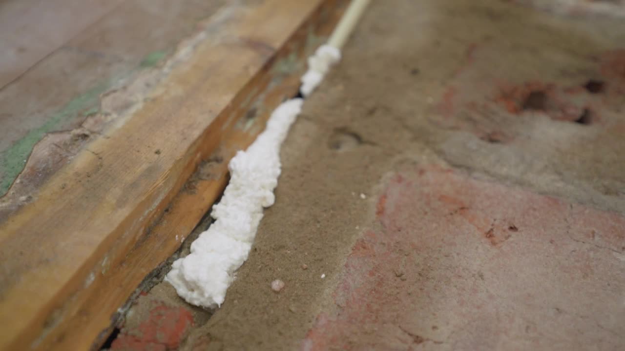 一名工人用泡沫泡沫地板的接缝。一个人在安装泡沫塑料的帮助下修补地板。用安装泡沫修复地板。工人用安装泡沫填充房间墙壁和水泥地面之间的裂缝。视频素材