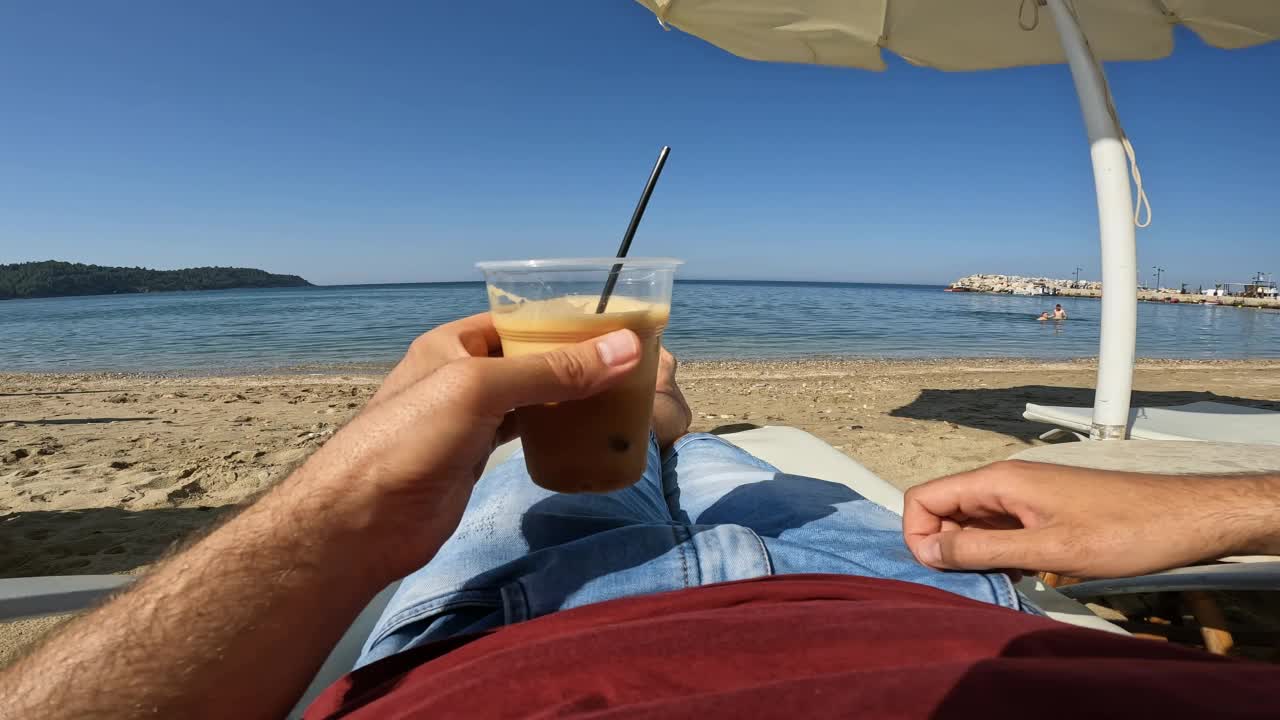 喝着冰咖啡的男人在海滩的躺椅上放松视频素材