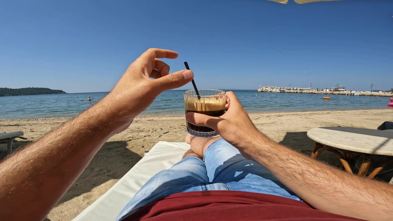 喝着冰咖啡的男人在海滩的躺椅上放松视频素材
