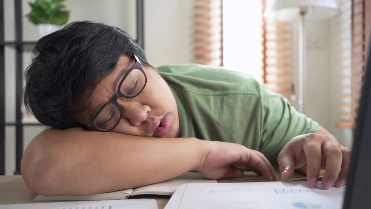 试过一个亚洲人在家用笔记本电脑工作时睡在桌子上。在自由职业中工作到最后期限视频素材