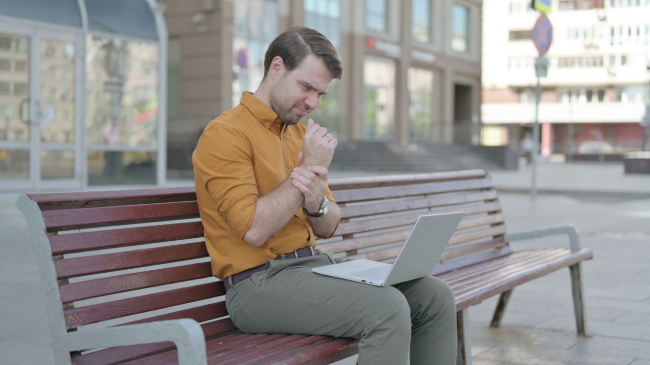 年轻人坐在长凳上使用笔记本电脑时手腕疼痛视频下载