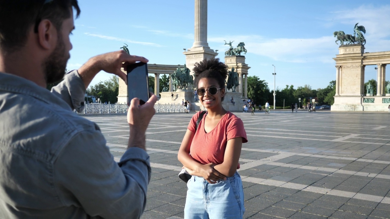情侣们在夏天旅行，一起在城市里享受假期，在地标附近用手机拍照视频素材