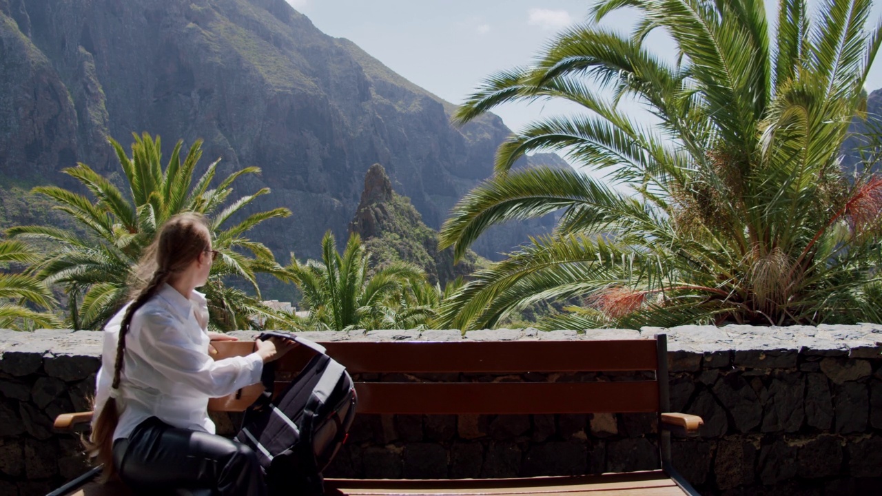 马斯卡峡谷和特内里费岛上的村庄。背着背包的女孩坐在长椅上欣赏风景。慢动作视频素材