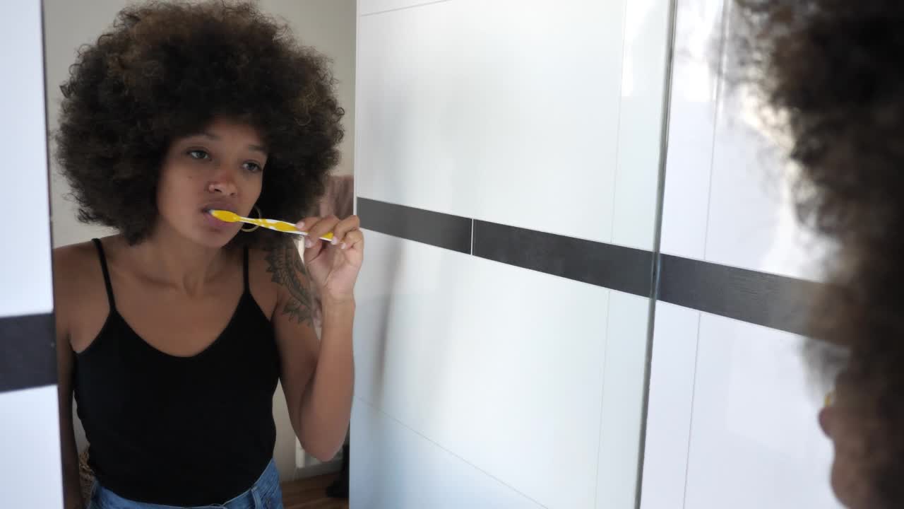 非洲裔美国妇女在浴室对着镜子刷牙视频素材