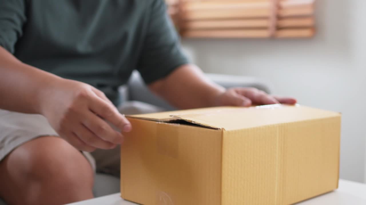 快乐的男人坐在沙发上打开收到的盒子，微笑着看里面视频素材