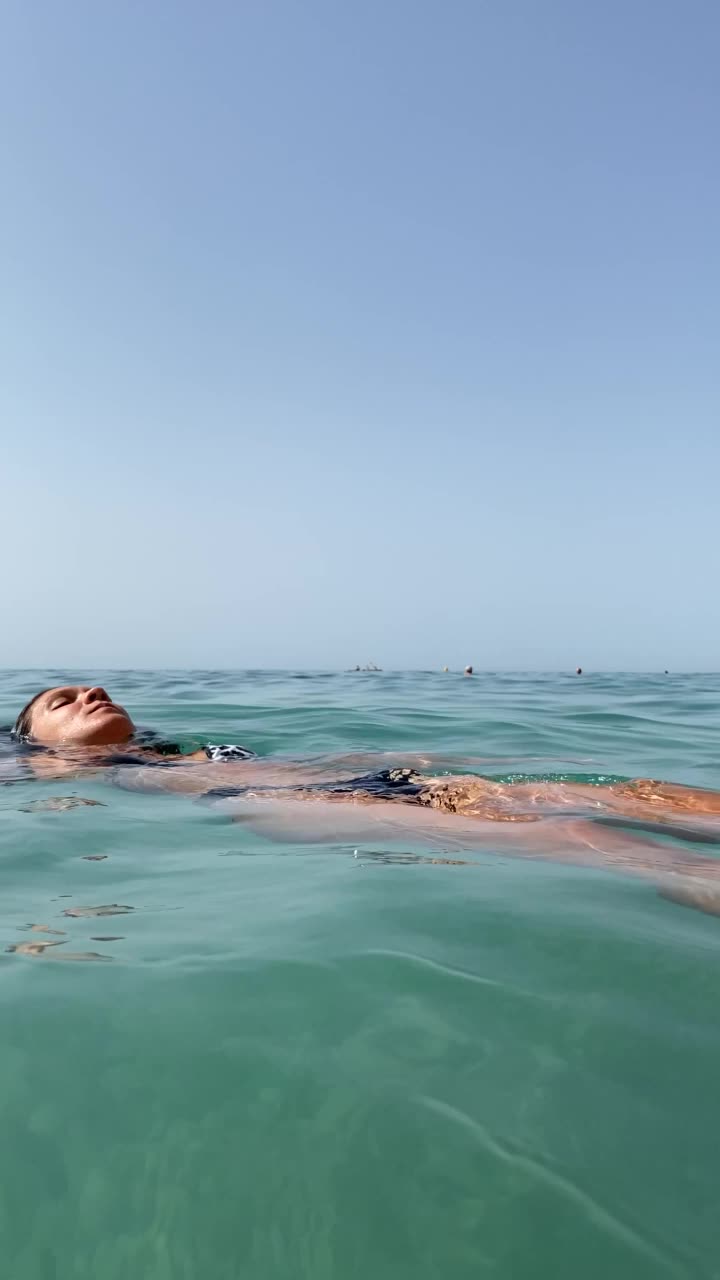 女人在海里洗澡和玩死在水中放松和阳光明媚的日子在海滩上晒太阳。小女孩享受在海浪中游泳的垂直视频。视频下载