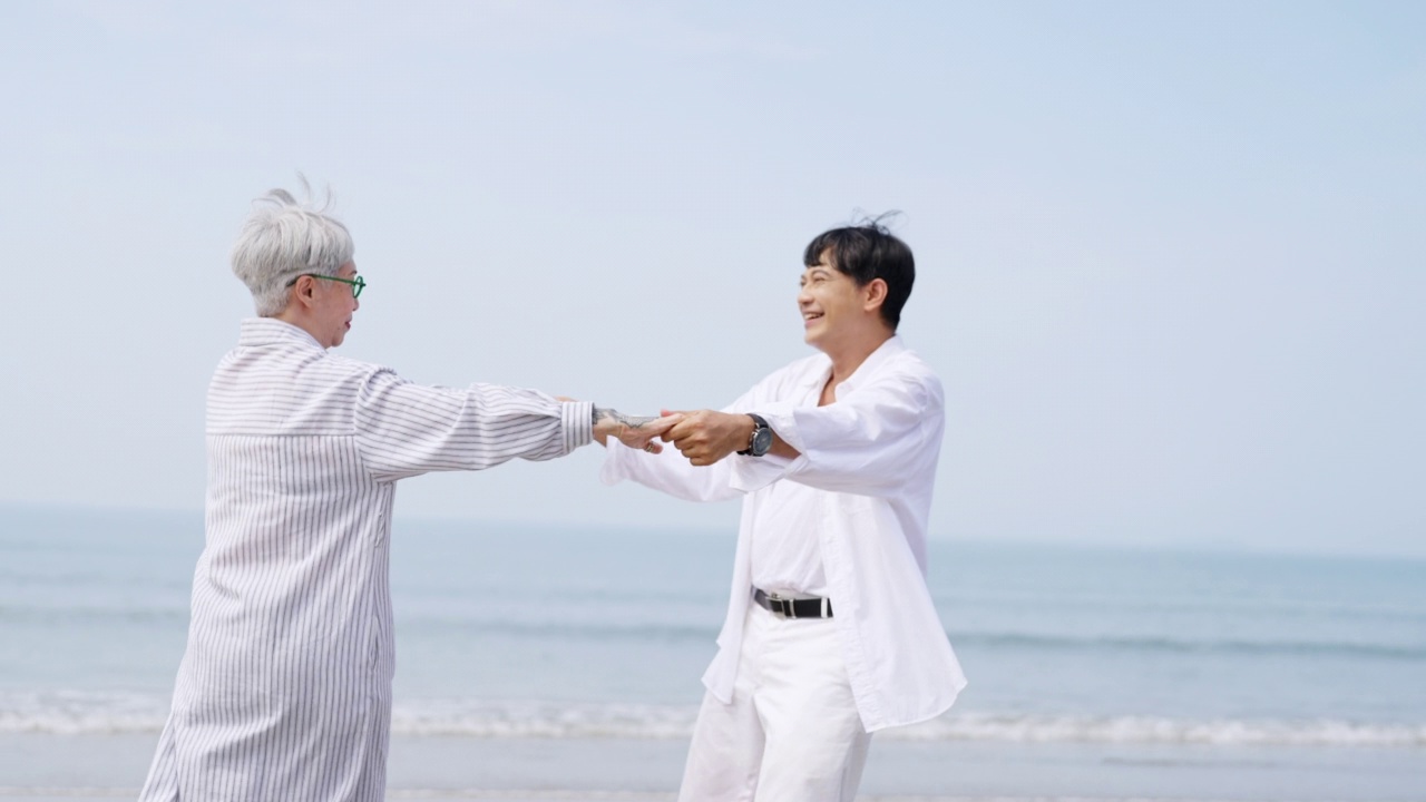 4K亚洲老年情侣在夏日夕阳下的海滩上一起跳舞。视频下载