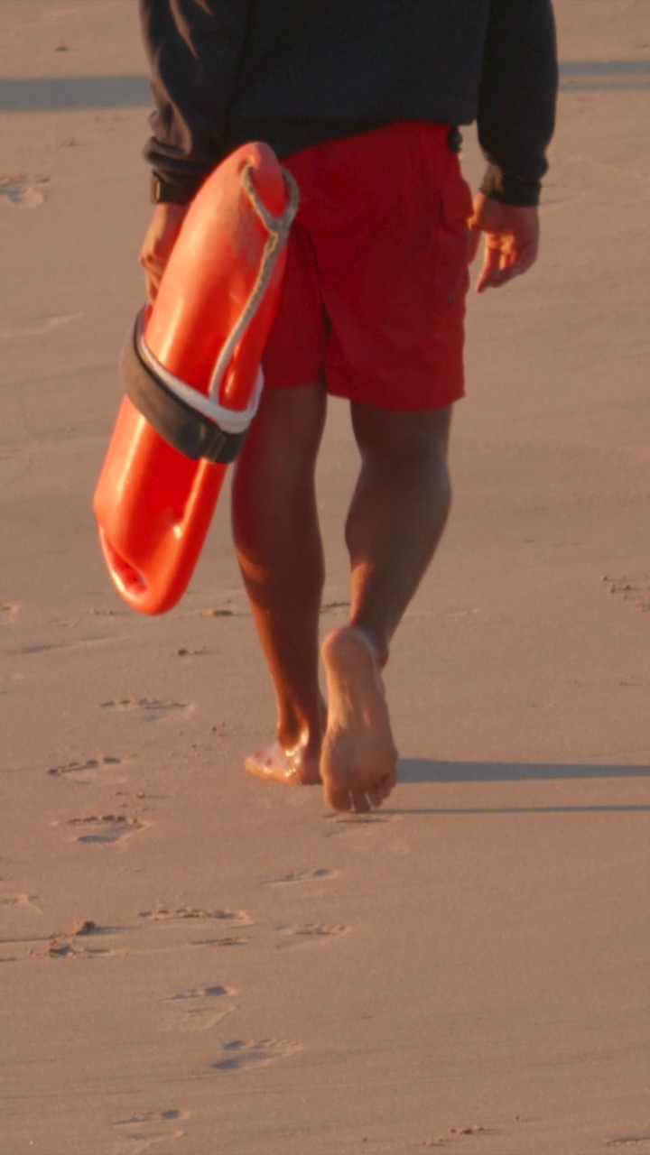 救生员巡逻行走在海滩上，带着红橙黄色救生罐。- - - - - -垂直格式视频下载