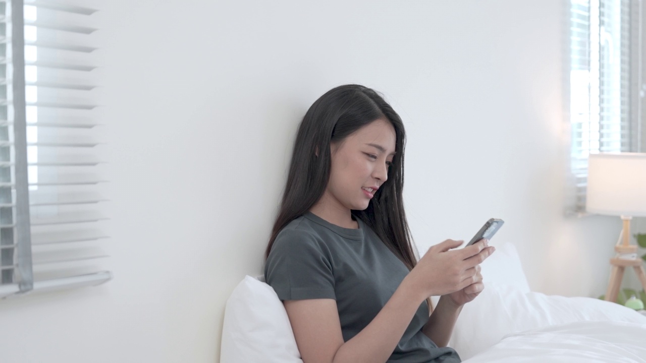 年轻美丽的亚洲女性使用智能手机上网或在家里与朋友聊天，放松和缓解压力。视频素材