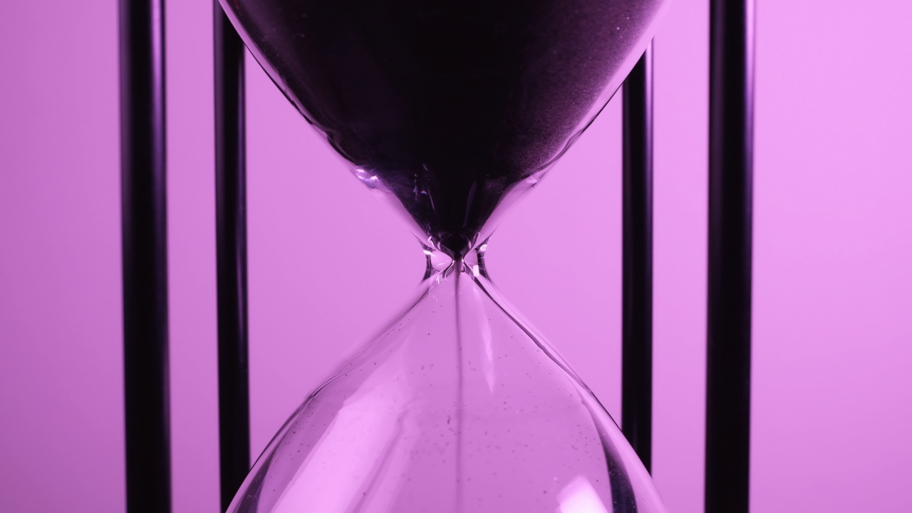 特写的沙子计时器时钟与沙子流动从沙漏在紫色色调。视频素材
