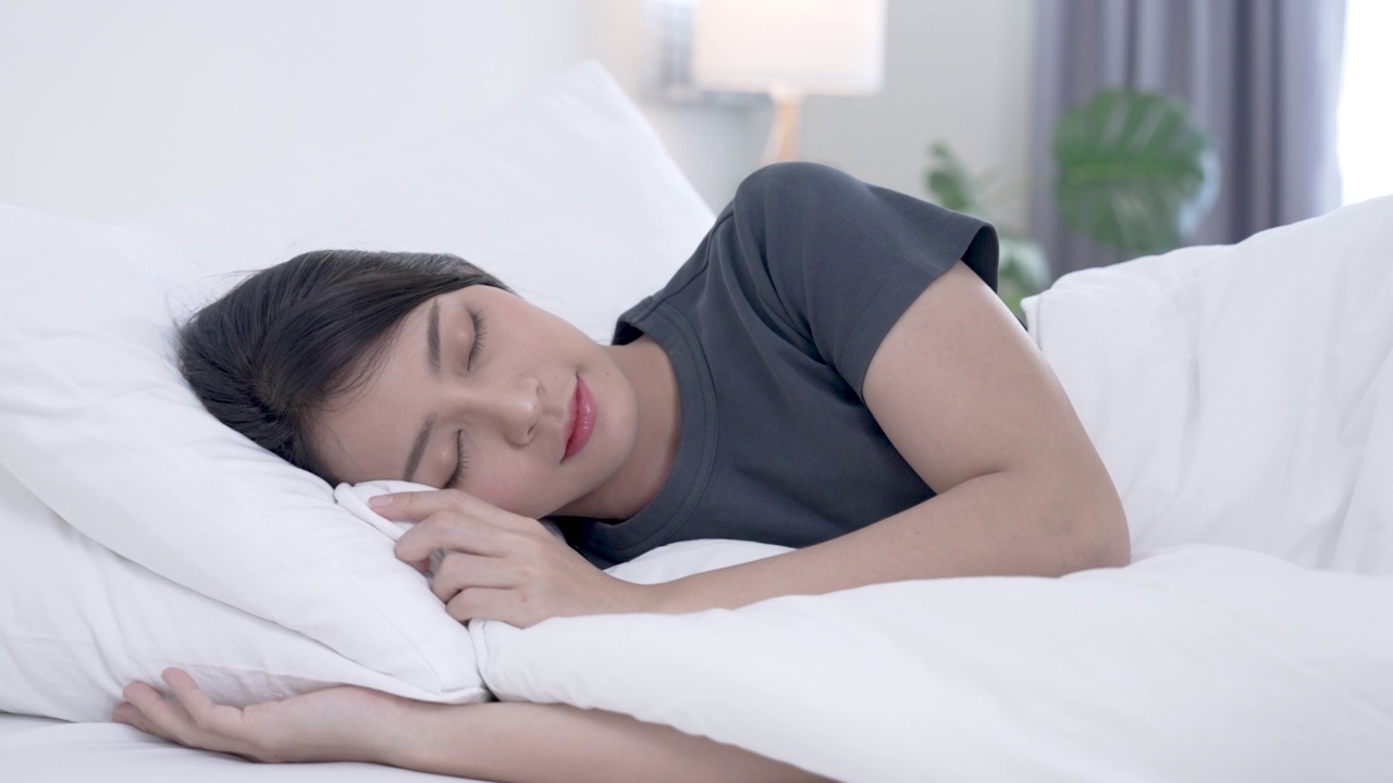 年轻美丽的亚洲女人在早上的床上快乐地睡觉。视频素材