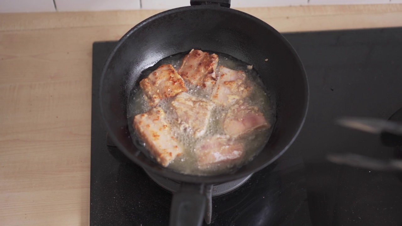 在家里厨房用油锅煎炸五花肉。不健康的亚洲食物，高胆固醇的肉类晚餐准备视频素材
