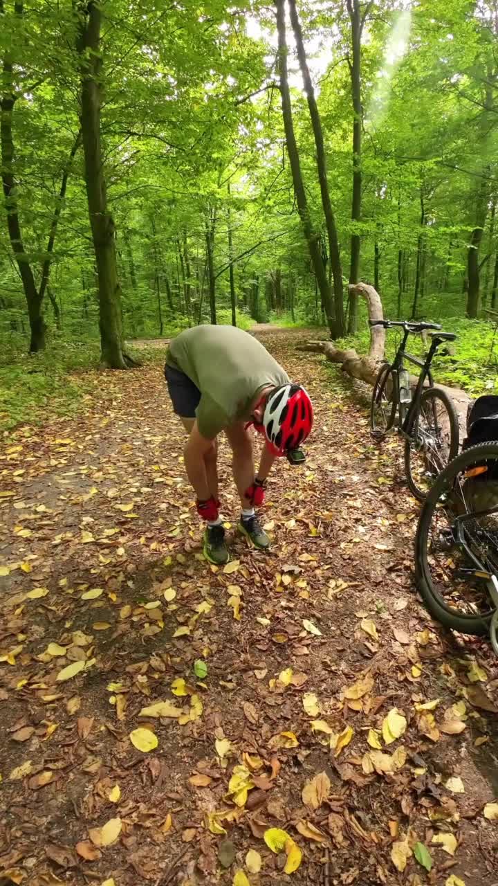 一名戴着防护头盔的男子在森林里骑自行车前整理袜子。视频下载