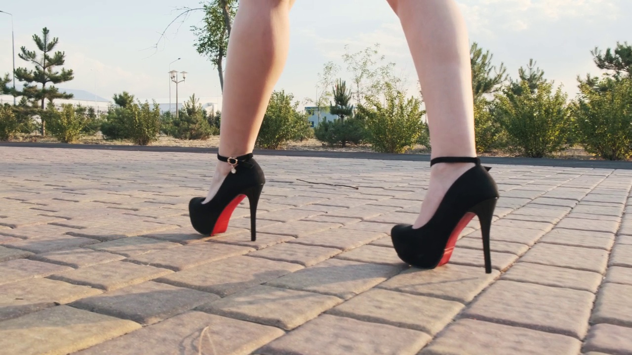 阳光明媚的日子里，穿着黑色高跟鞋的女性修长的双腿走在公园里。一个优雅的女孩在走。低角度，慢镜头，特写视频素材