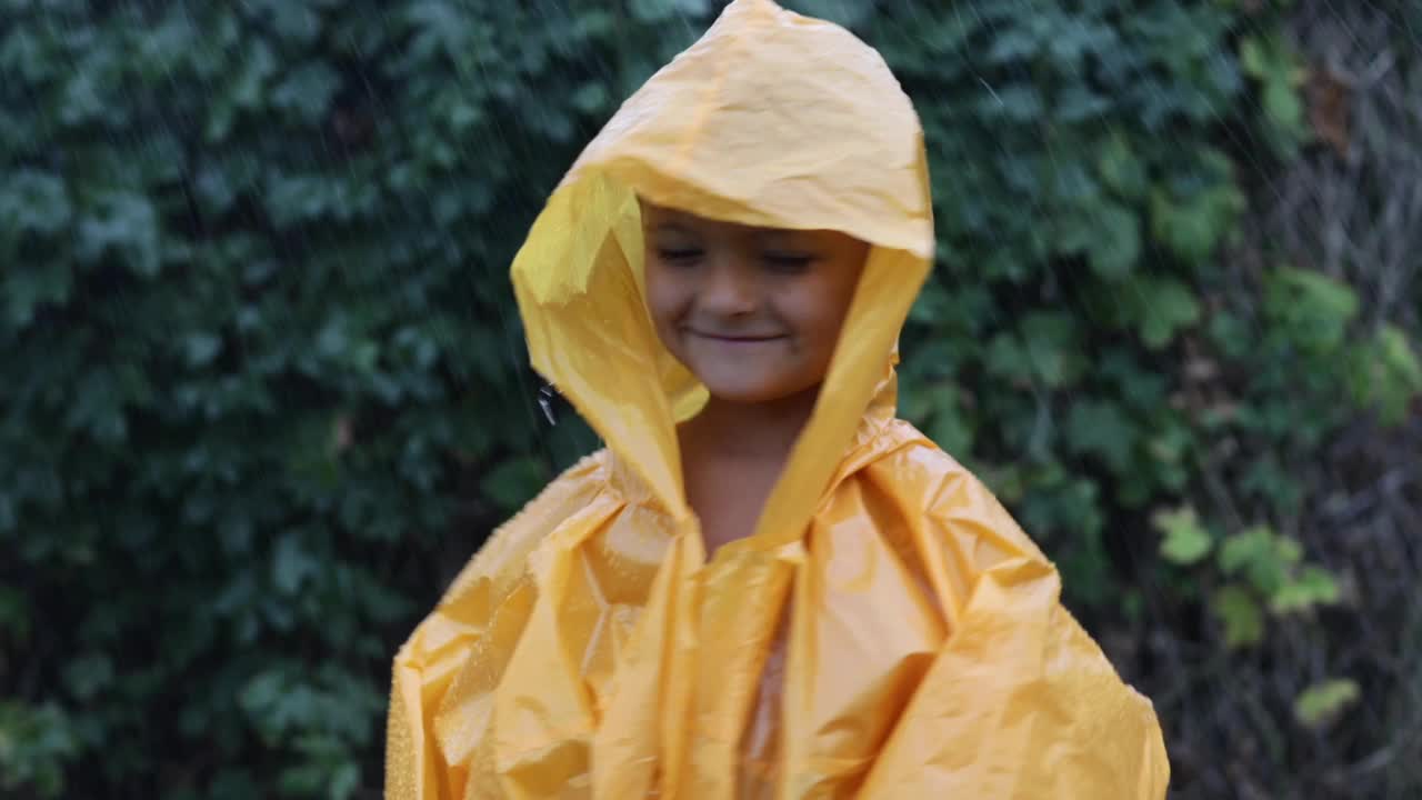 一个小男孩穿着雨衣站在雨中。夏天的雨滴在穿雨衣的人身上。孩子们对气候变化的喜悦视频下载