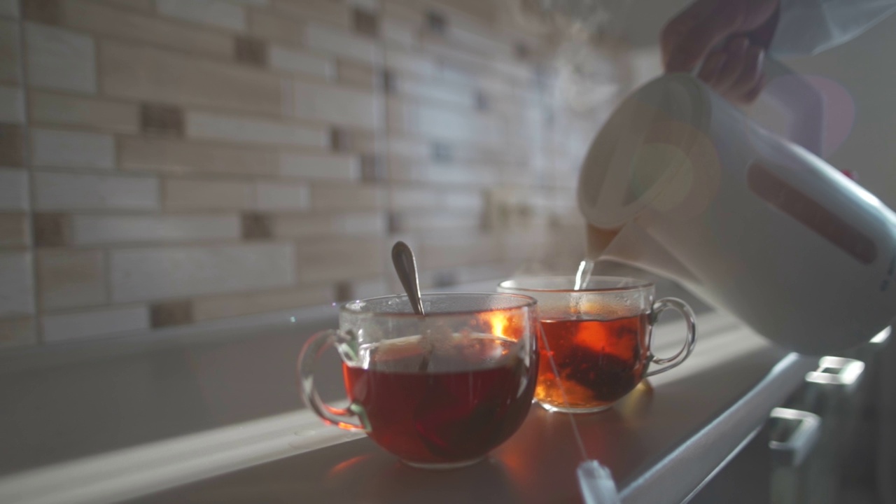 女人把热水从茶壶里倒进一个有茶包的杯子里。舒适的心情和完美的早晨。视频素材
