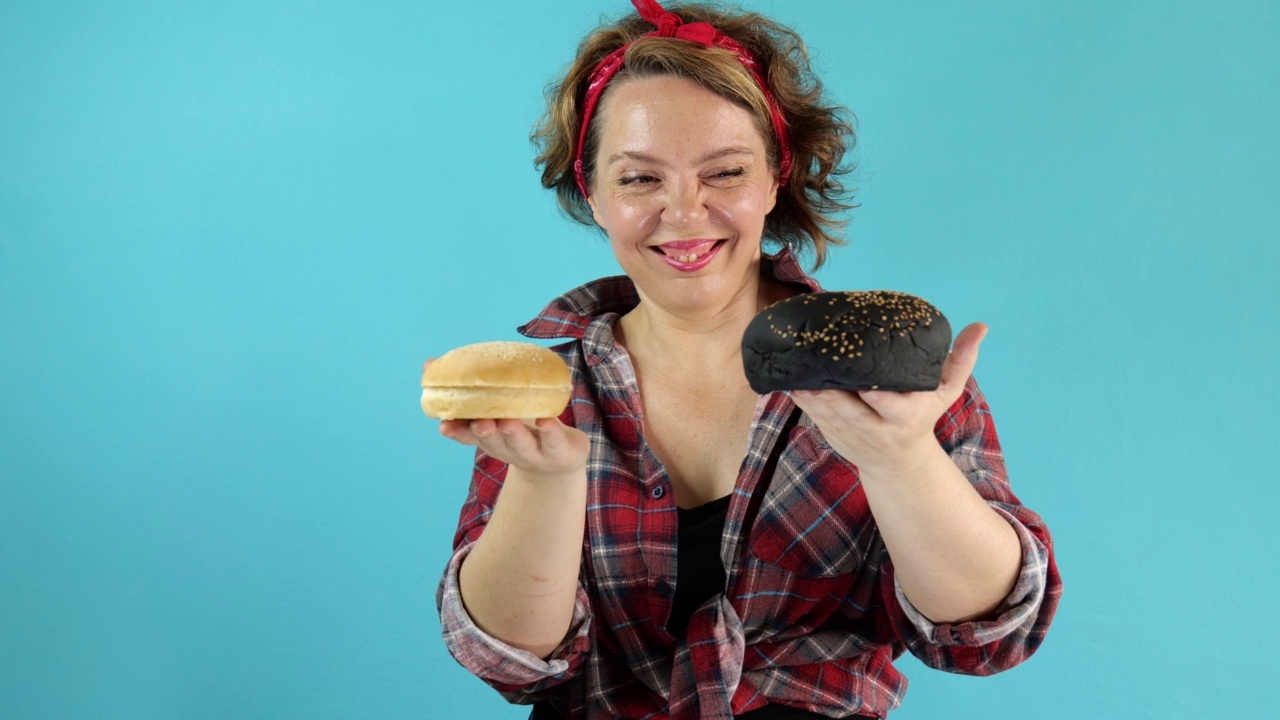 四十岁的海报女郎穿着格子衬衫，手里拿着一个黑白相间的汉堡面包，背景是孤立的蓝色。一个成年女性的肖像。销了风格视频下载