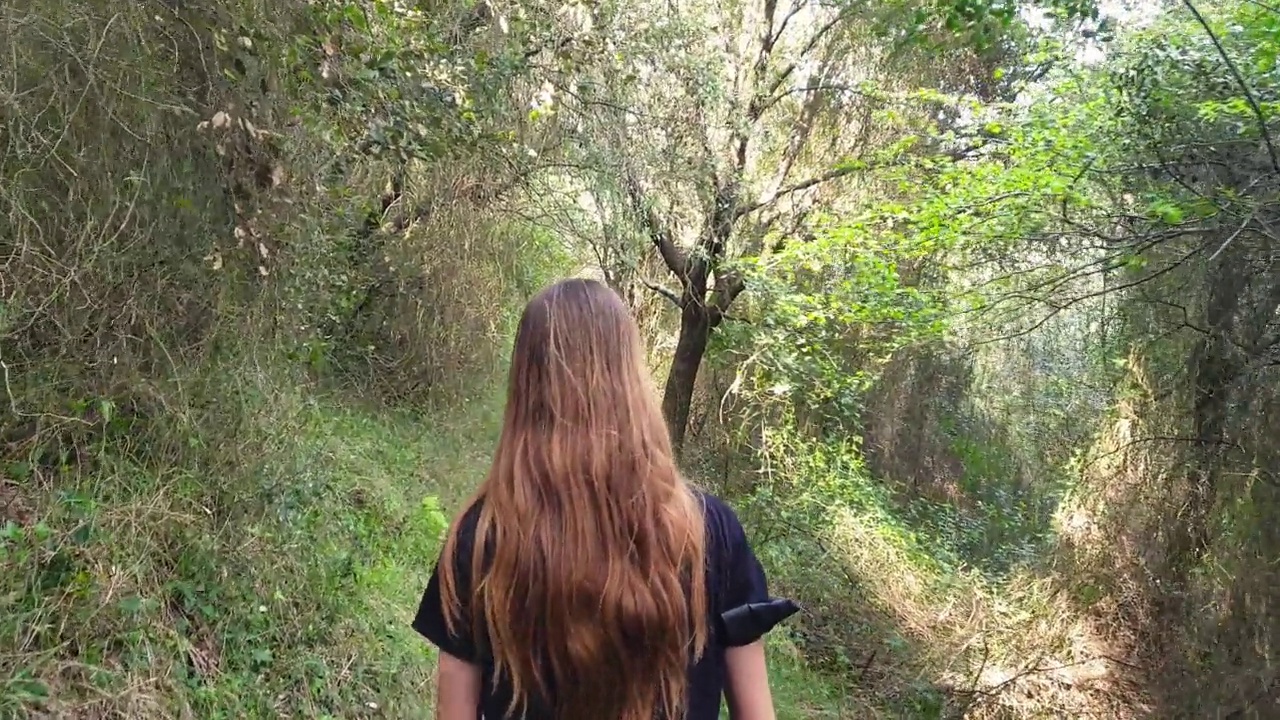 十几岁的女孩，棕色长发，穿着黑色运动服在自然中行走视频素材