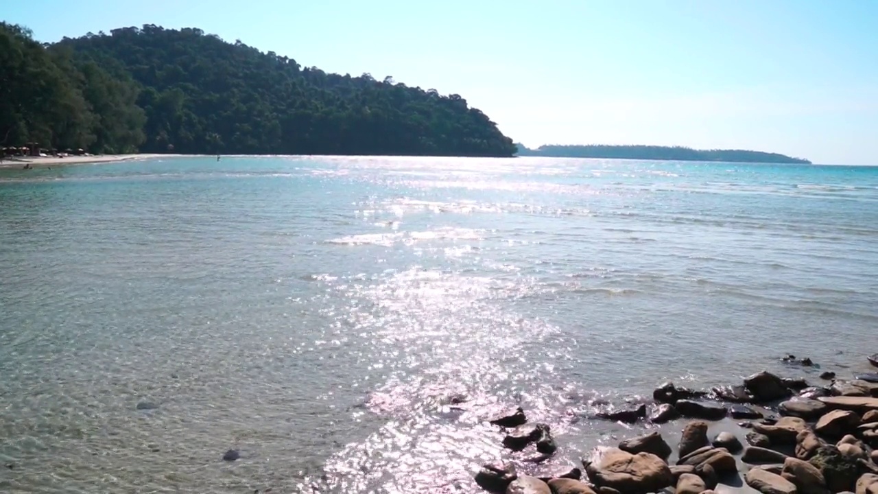 简单的海滩岩石海与山和阳光反射在波水。视频素材